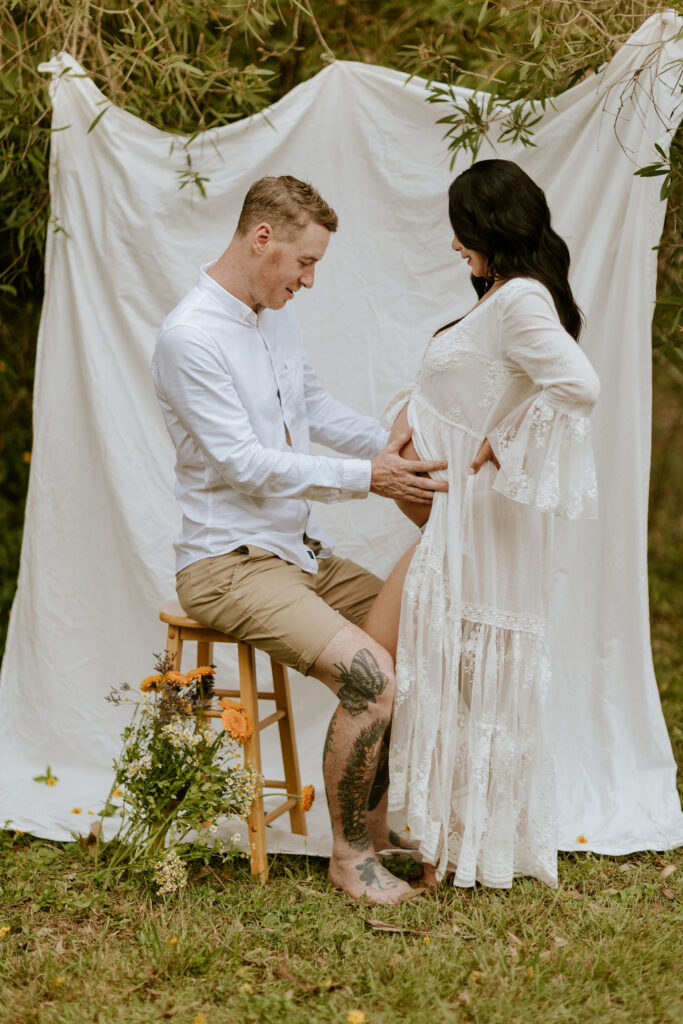 Pregnant couple during Brisbane maternity photoshoot at home with linen backdrop and market flowers