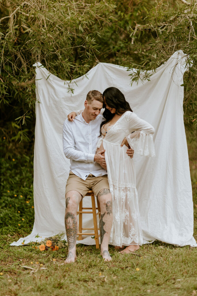 Pregnant couple during Brisbane maternity photoshoot at home with linen backdrop and market flowers